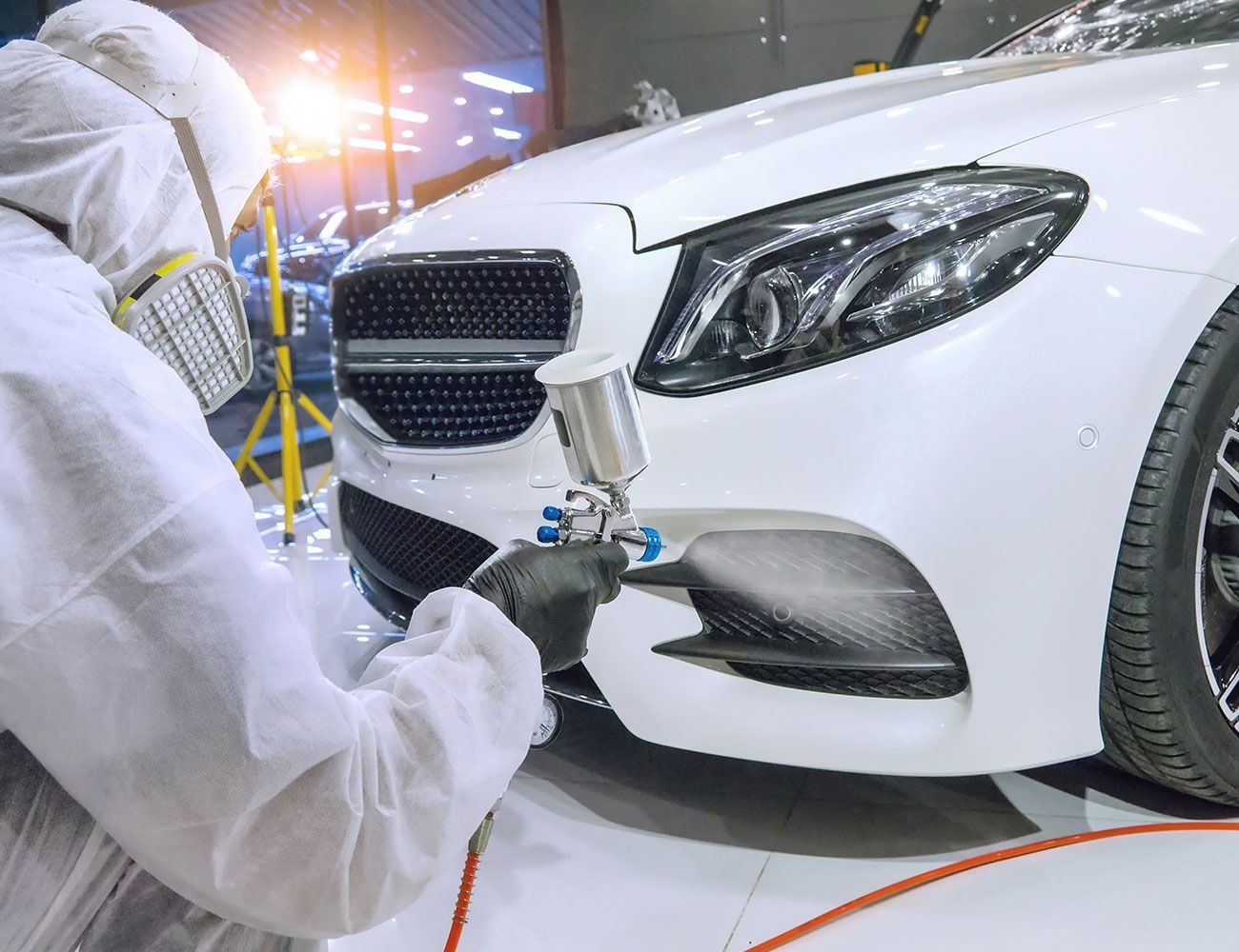 Ein Lackierer lackiert mit einer Sprühmaschine ein weises Auto