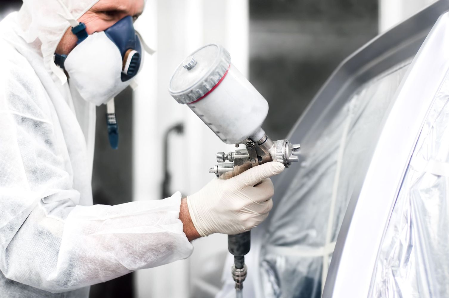 Ein Lackierer lackiert mit einer Sprühmaschine ein Auto